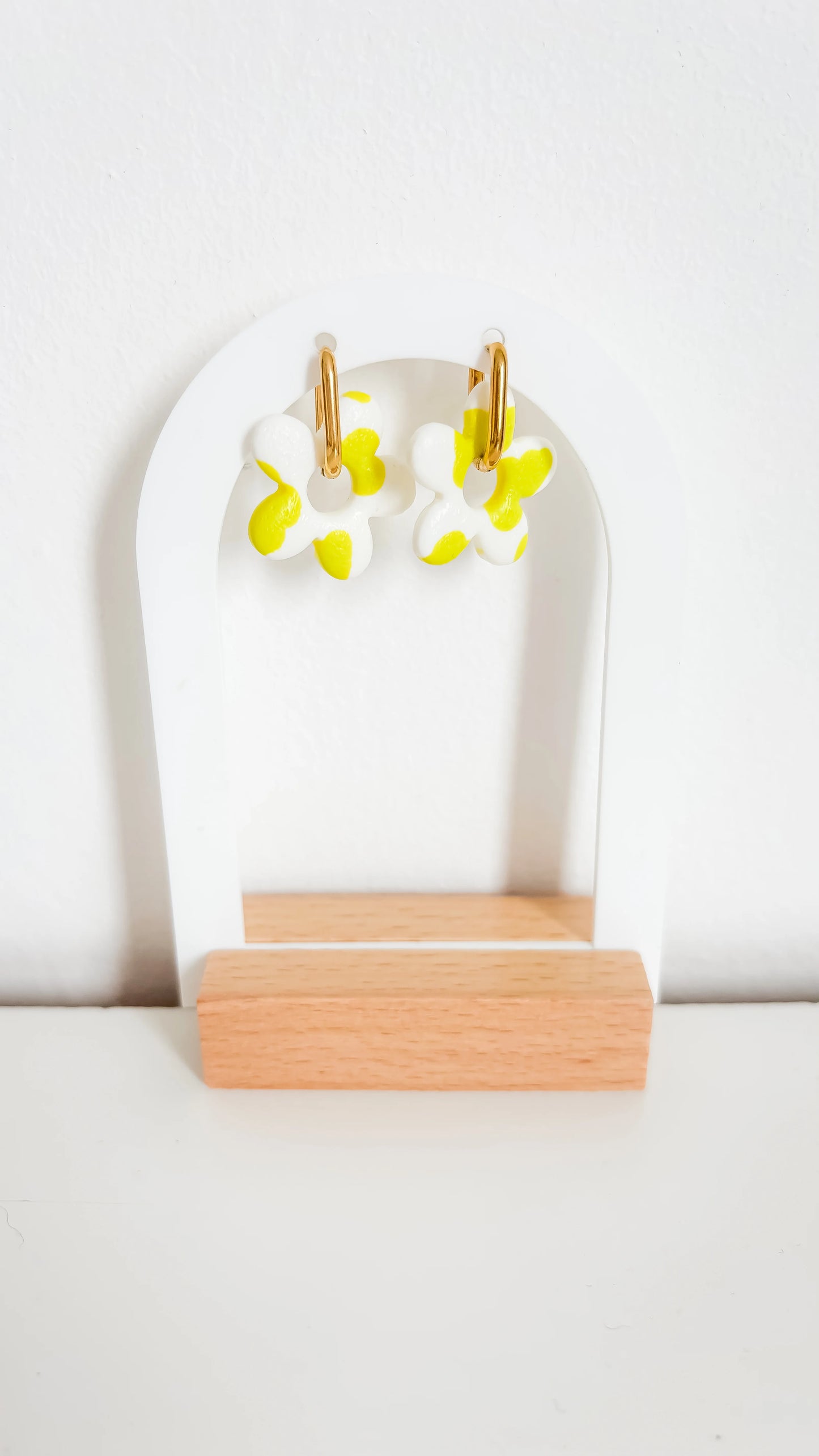 Boucles d’oreilles fleuries jaunes et blanches sur créoles plaquées or, photographiées de face sur un support design.