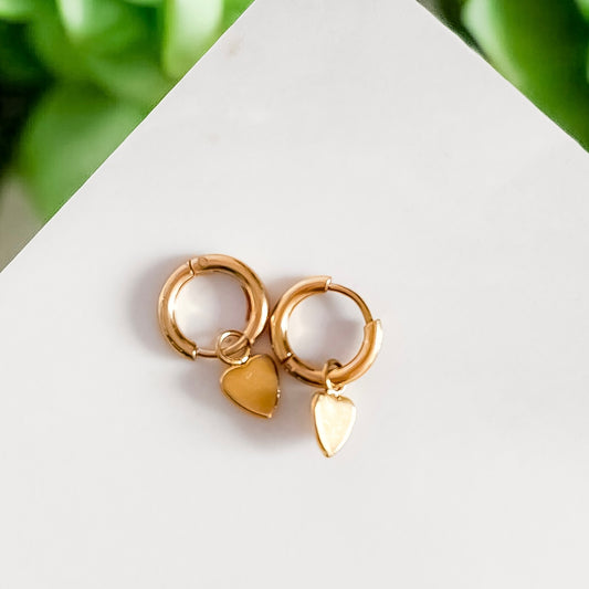 Photo d'une paire de boucles d'oreille créoles plaquée or avec un petit coeur accroché aux deux boucles