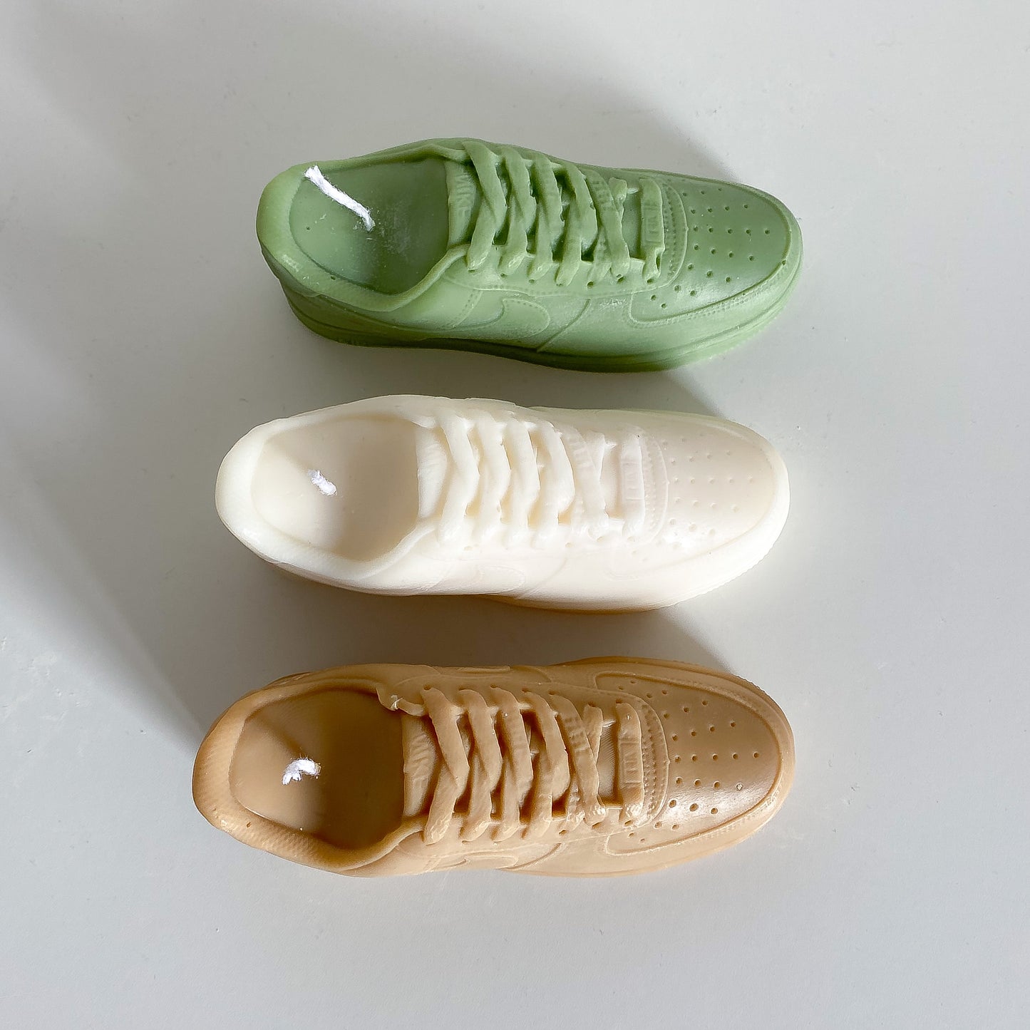 plusieurs bougies air force 1 en différents coloris : l'une marron, la seconde blanche et la dernière verte