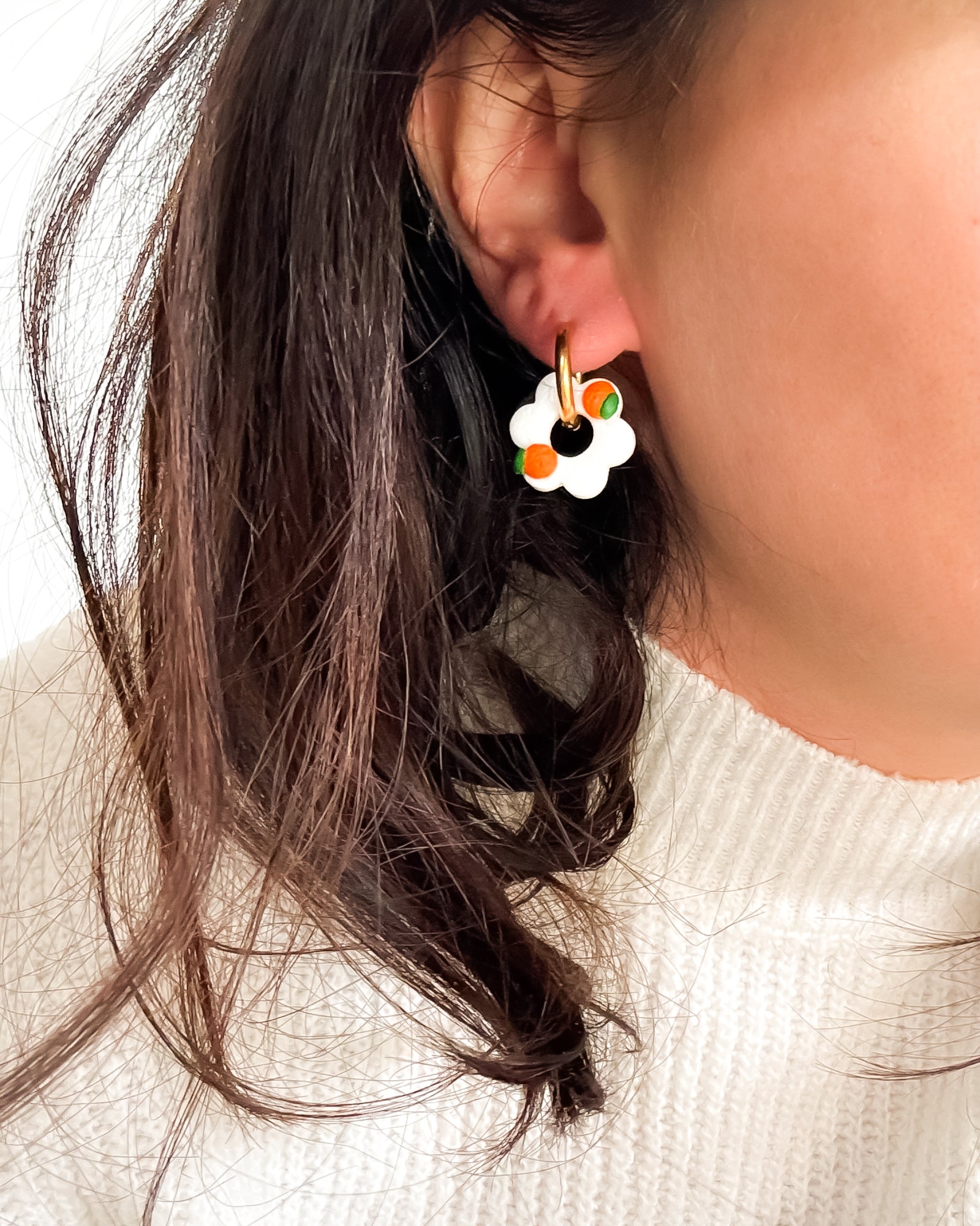 Une boucle d'oreille créole en forme de fleur avec des motifs fruits (orange), portée par une femme