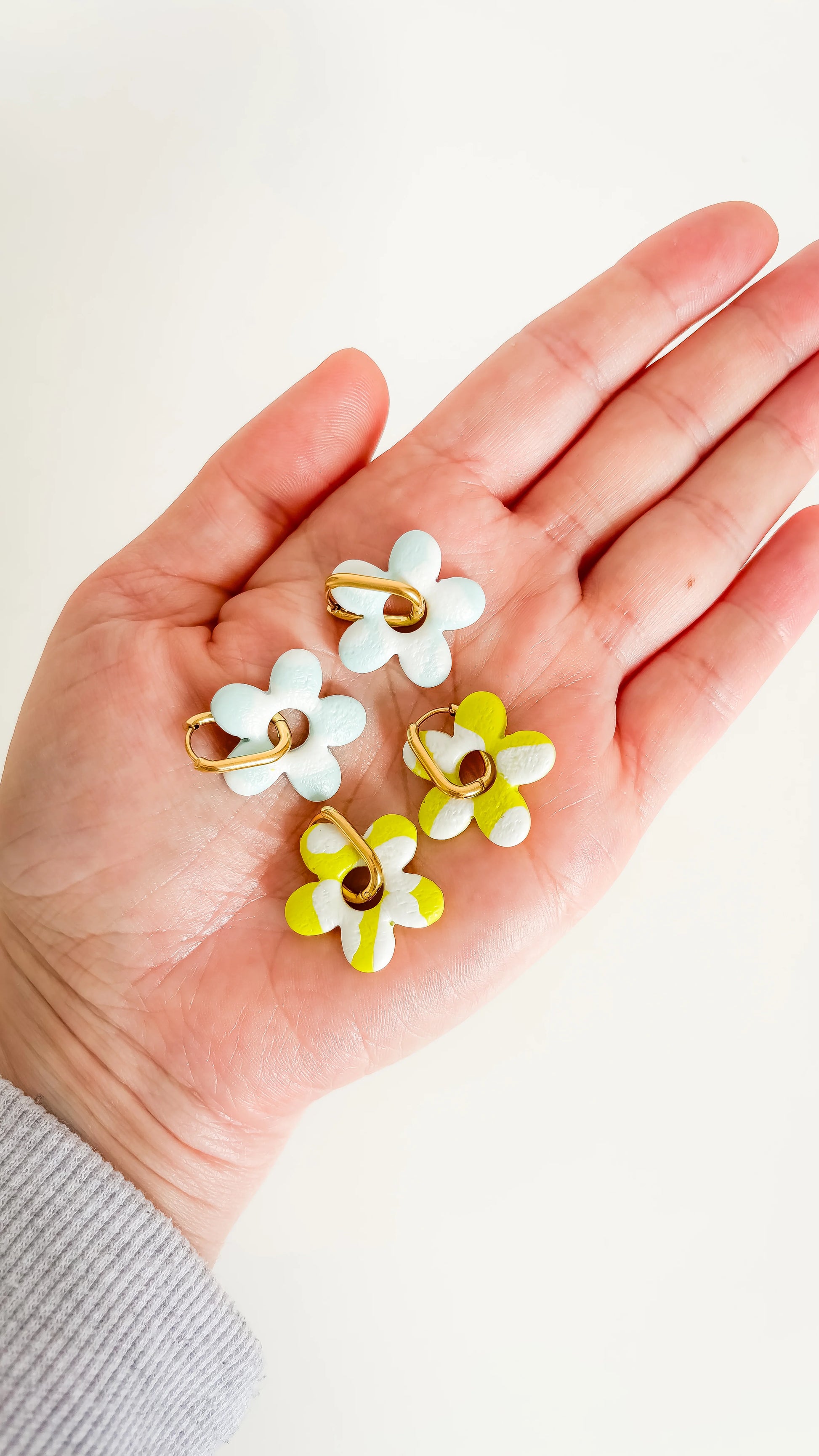  Charms en forme de fleurs bleu pastel et jaune citron, posés dans une main, prêtes à être assemblées sur des créoles.