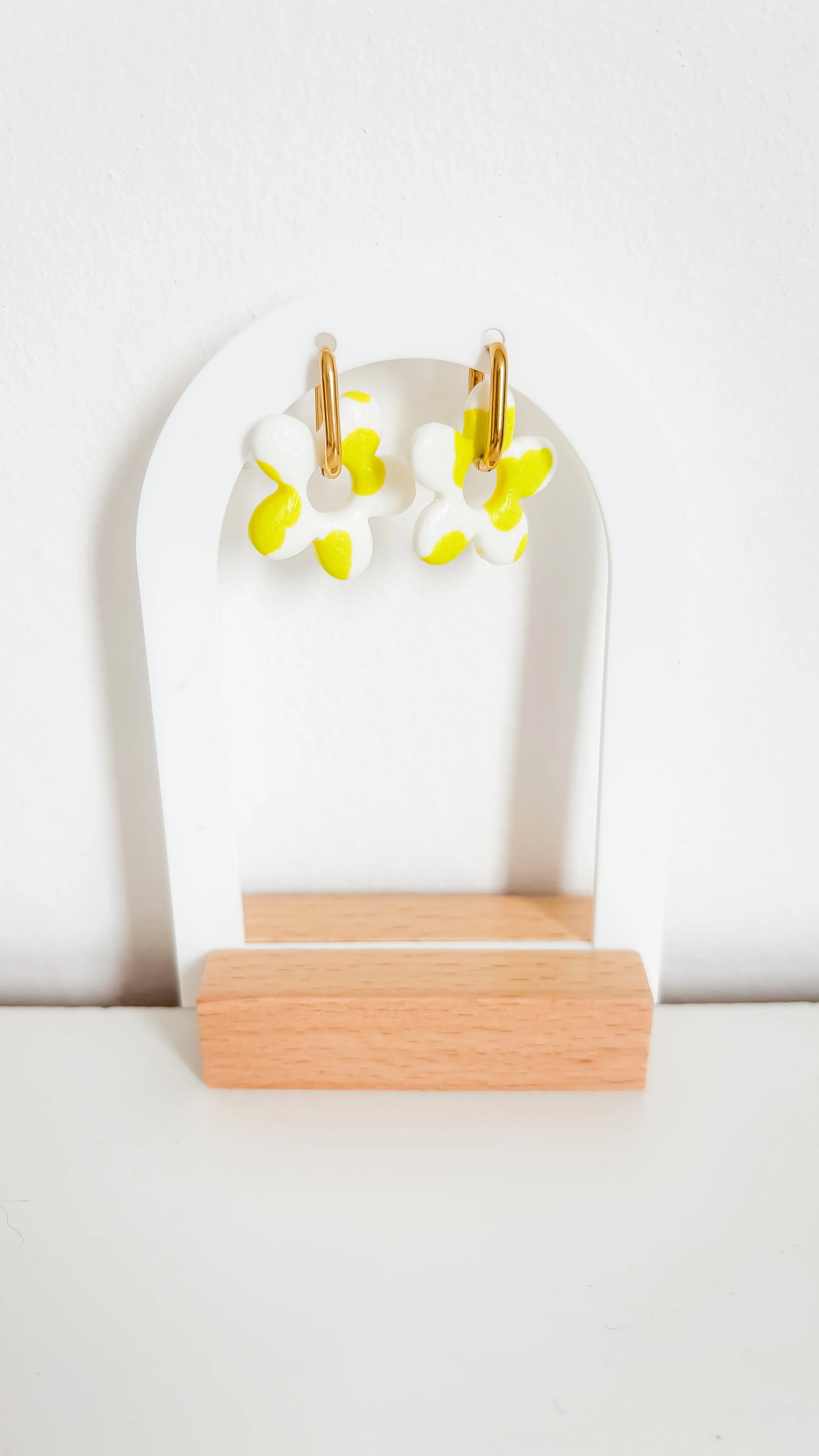 Boucles d’oreilles fleuries jaunes et blanches sur créoles plaquées or, photographiées de face sur un support design.