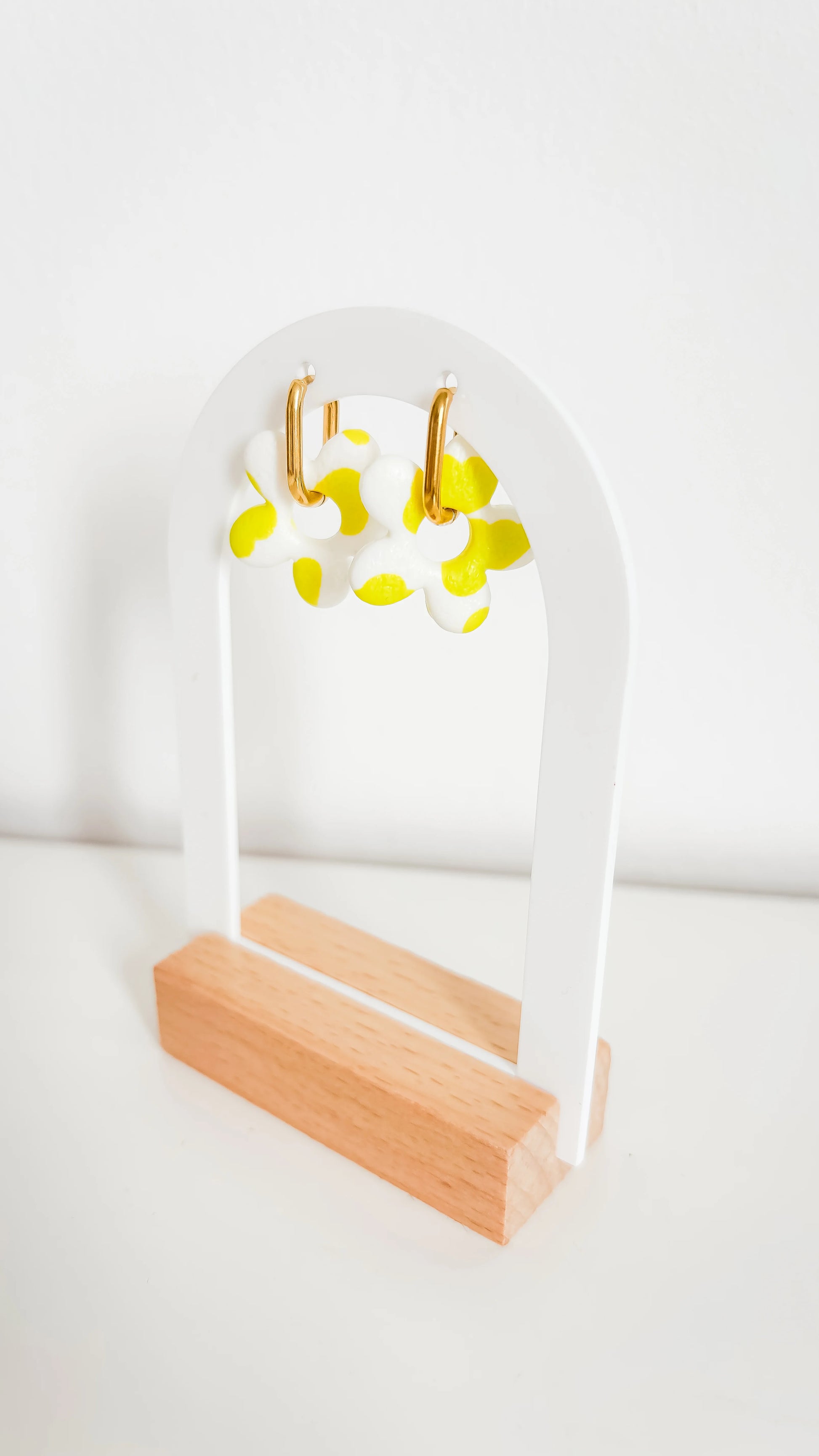 Boucles d’oreilles fleuries jaunes et blanches sur créoles plaquées or, photographiées de biais sur un support design.