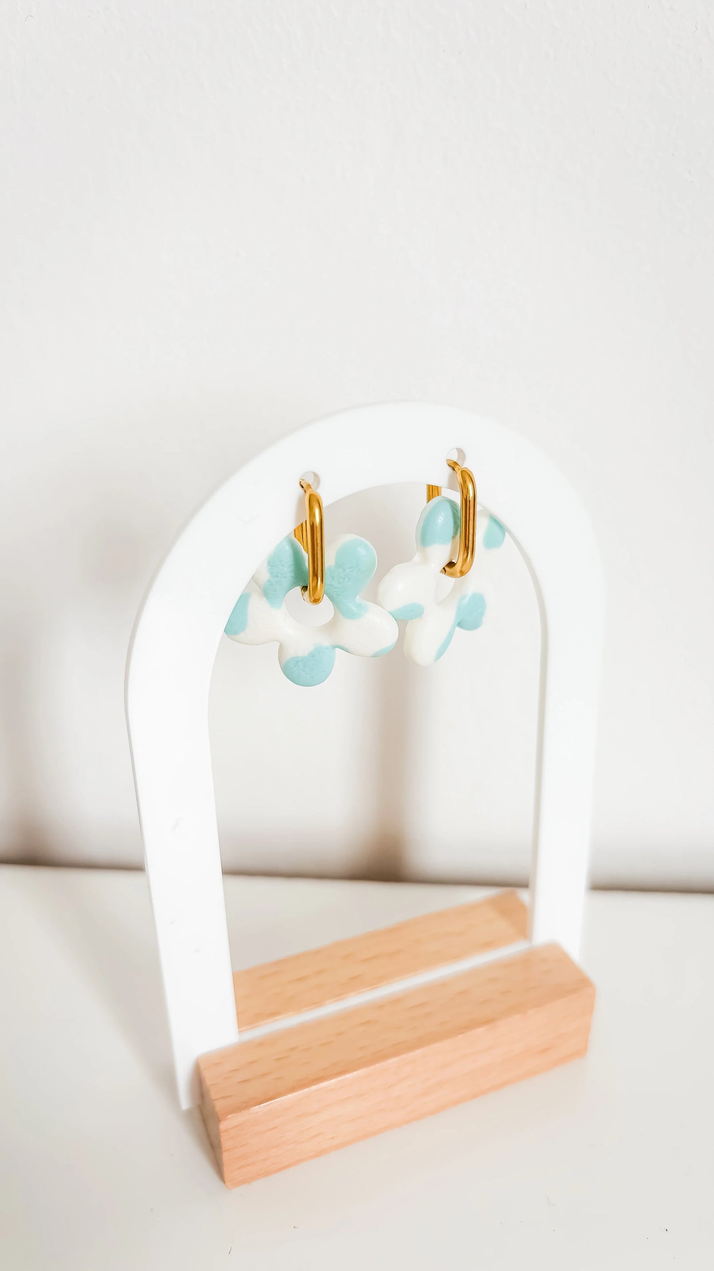 Boucles d’oreilles fleuries bleues et blanches sur créoles plaquées or, photographiées de biais sur un support design.