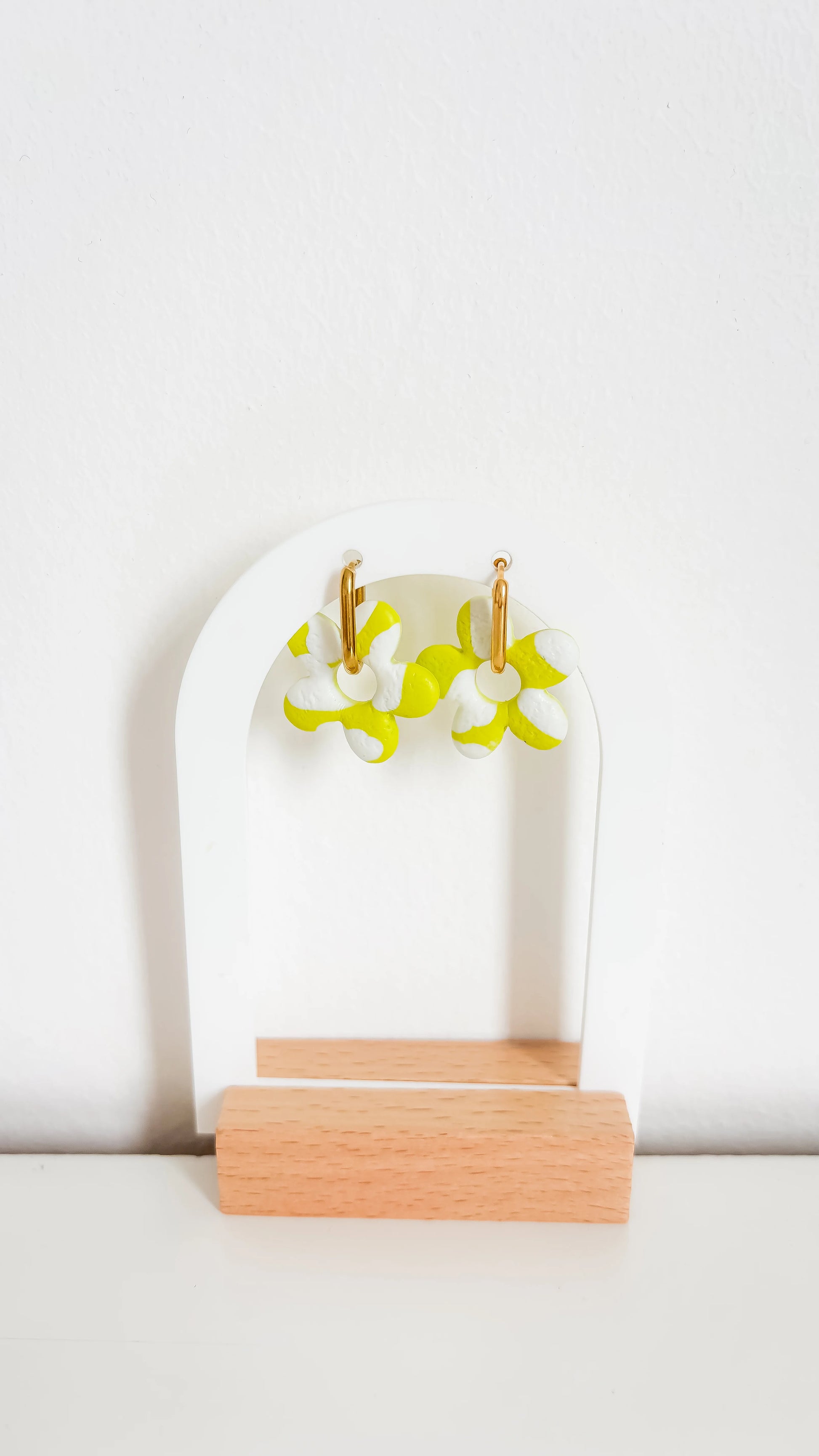 Boucles d’oreilles fleuries jaunes et blanches sur créoles plaquées or, de face sur un support design.