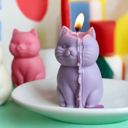 Photo d'une bougie violette allumée en forme de chat, avec une autre bougie chat rose en arrière-plan