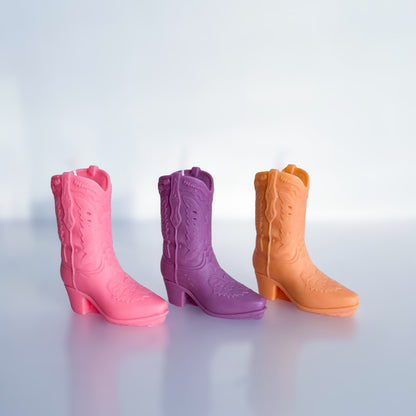 3 bougies santiags posées côte à côté : l'une est rose, la seconde violette, la troisième orange