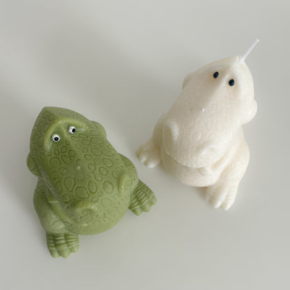 Photo d'une bougie dinosaure verte posée à côté d'une bougie dinosaure blanche