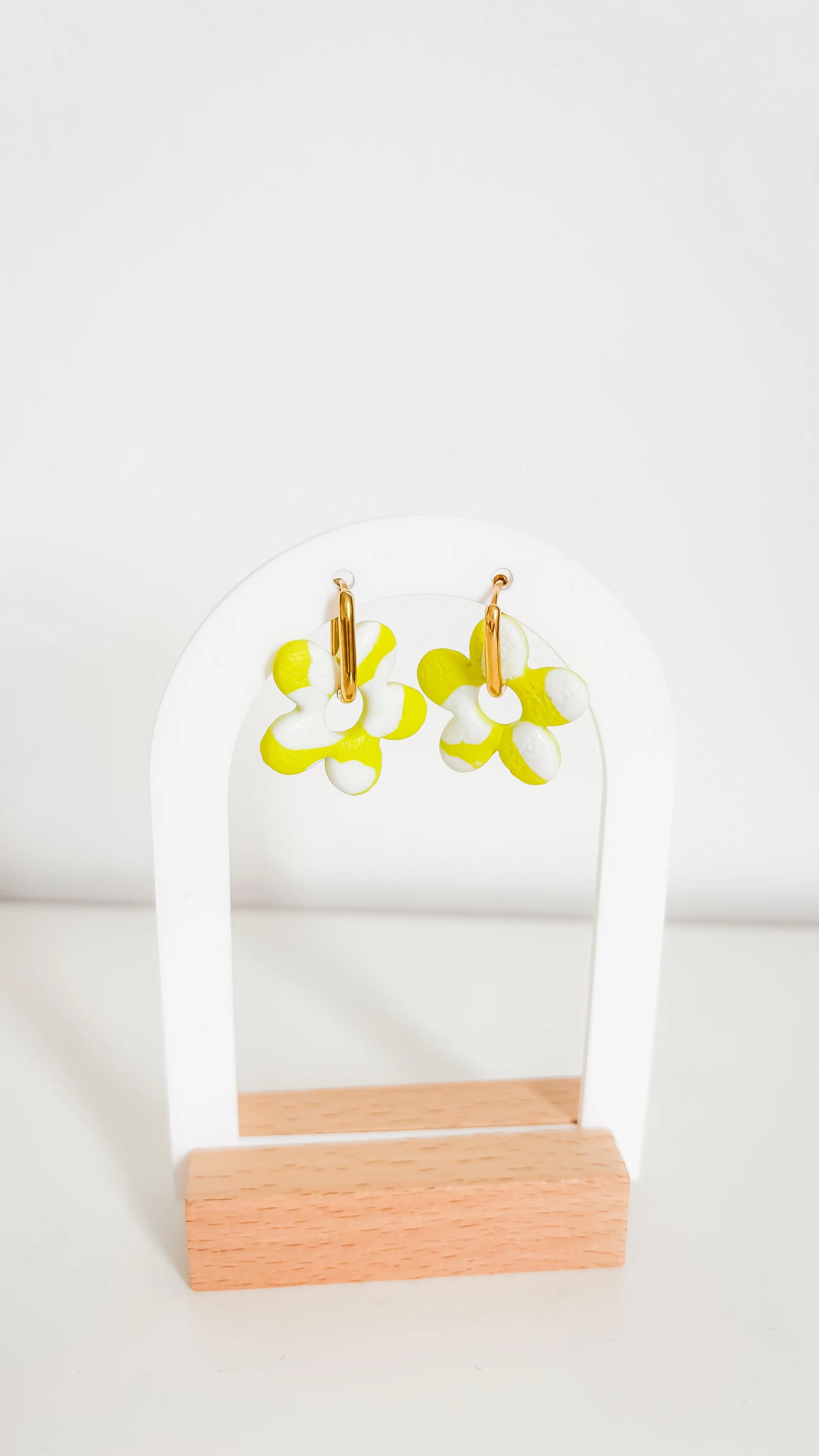 Boucles d’oreilles fleuries jaunes et blanches sur créoles plaquées or, photographiées légèrement de biais sur un support design.